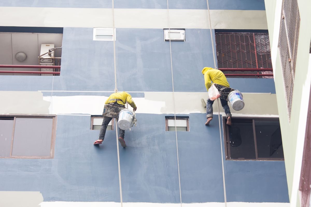 painters hanging on roll, painting color on building wall.
facade builder worker with roller brush, working on high building.
safety construction with lift rope belt in city.